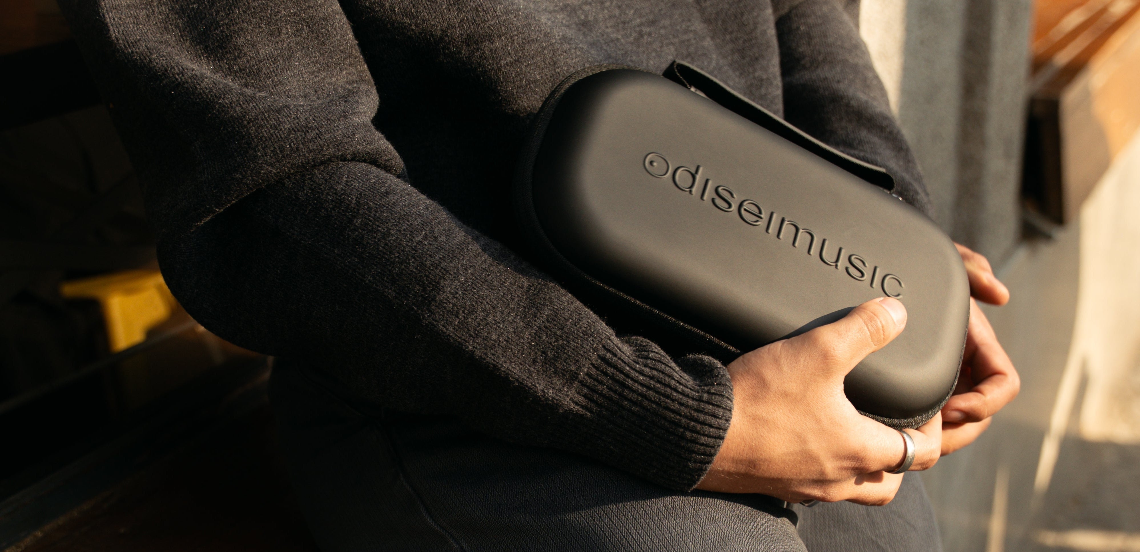 Person holding a black 'odiseimusic' product case with a blurred background